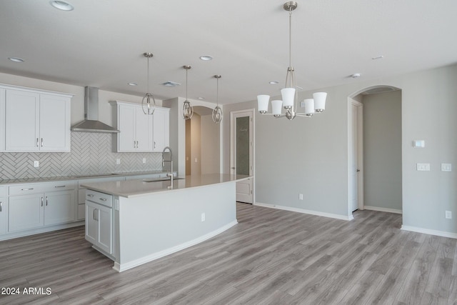 kitchen featuring an island with sink, a sink, wall chimney exhaust hood, stovetop, and arched walkways