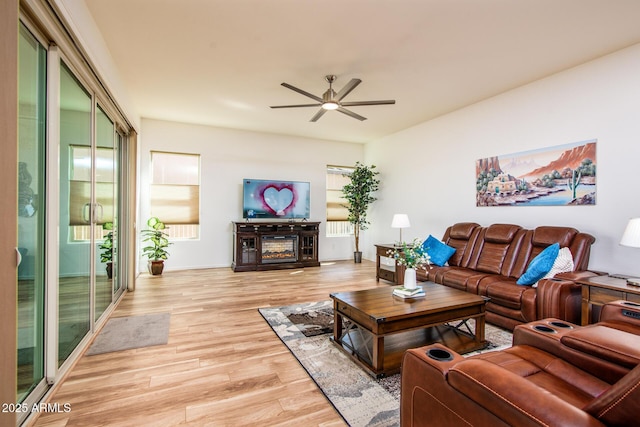 living room featuring light wood-style floors, a glass covered fireplace, and a ceiling fan