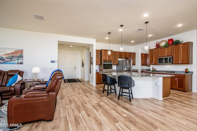 kitchen featuring light stone counters, a breakfast bar area, decorative light fixtures, appliances with stainless steel finishes, and a center island with sink