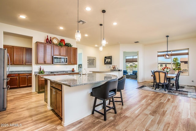 kitchen with visible vents, an island with sink, light stone countertops, stainless steel appliances, and pendant lighting