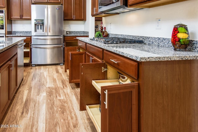 kitchen featuring stainless steel appliances, light stone counters, brown cabinetry, and light wood-type flooring