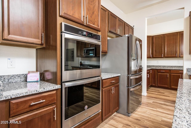 kitchen with stainless steel appliances, brown cabinets, light wood-style flooring, and light stone counters