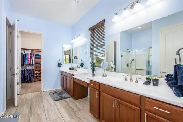 bathroom with double vanity, a shower stall, a spacious closet, and a sink