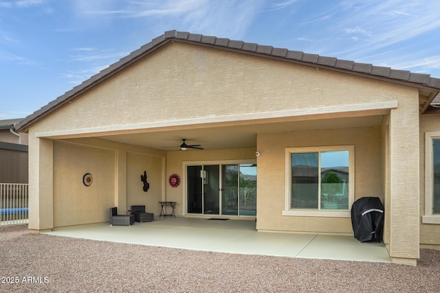 rear view of house with stucco siding, ceiling fan, fence, and a patio