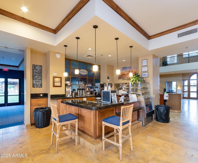 kitchen featuring visible vents, a breakfast bar, decorative light fixtures, a peninsula, and crown molding