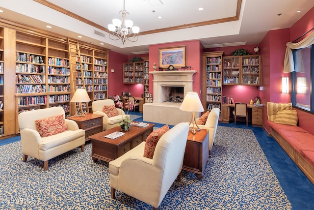 living area featuring a tray ceiling, crown molding, wall of books, and a tiled fireplace