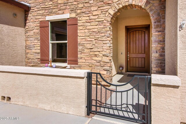 doorway to property with stone siding, a gate, and stucco siding