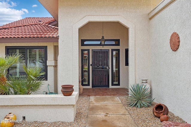 view of exterior entry with a tile roof and stucco siding