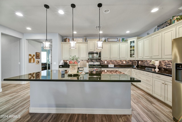 kitchen with backsplash, light hardwood / wood-style floors, pendant lighting, cream cabinetry, and appliances with stainless steel finishes