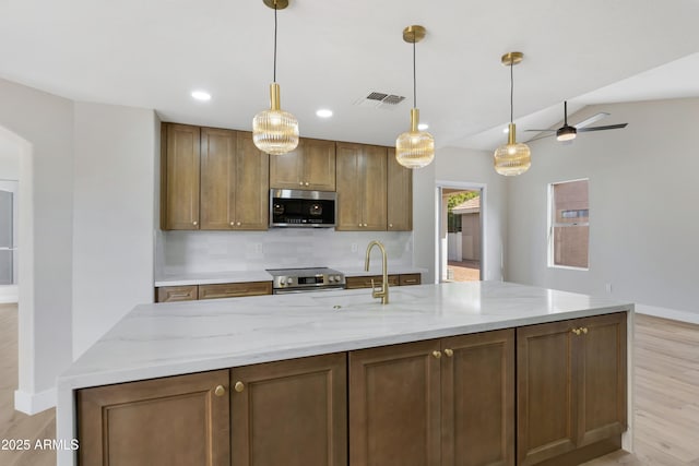 kitchen featuring ceiling fan, hanging light fixtures, light hardwood / wood-style floors, decorative backsplash, and appliances with stainless steel finishes