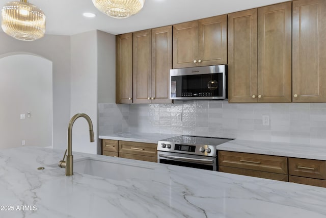 kitchen with sink, light stone counters, decorative light fixtures, decorative backsplash, and appliances with stainless steel finishes