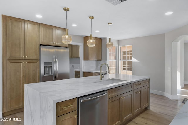 kitchen featuring sink, stainless steel appliances, light stone counters, an island with sink, and decorative light fixtures