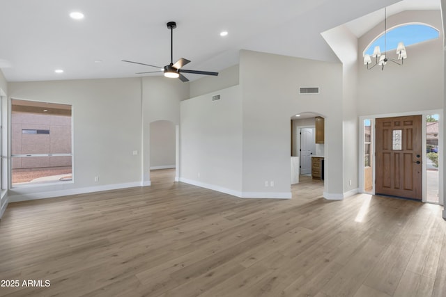 foyer with ceiling fan with notable chandelier, light hardwood / wood-style floors, high vaulted ceiling, and plenty of natural light