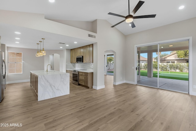 kitchen with a wealth of natural light, a center island with sink, stainless steel appliances, and decorative light fixtures