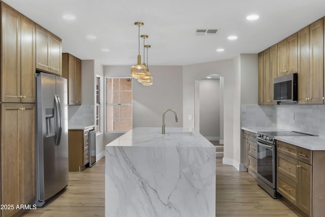 kitchen featuring backsplash, hanging light fixtures, sink, an island with sink, and appliances with stainless steel finishes