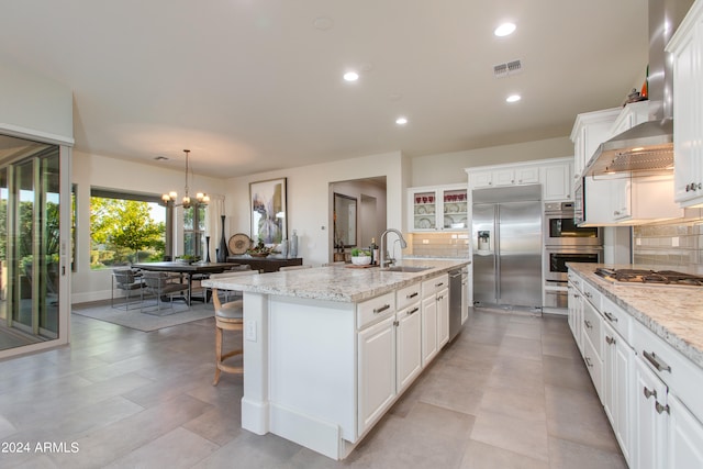 kitchen featuring hanging light fixtures, white cabinets, backsplash, stainless steel appliances, and a kitchen island with sink