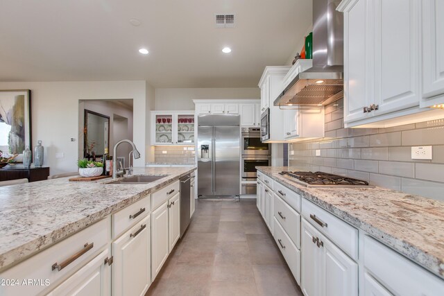 kitchen with white cabinets, built in appliances, sink, and wall chimney range hood