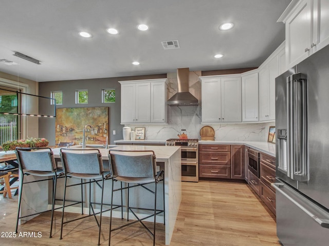 kitchen featuring white cabinetry, sink, stainless steel appliances, light wood-type flooring, and wall chimney exhaust hood