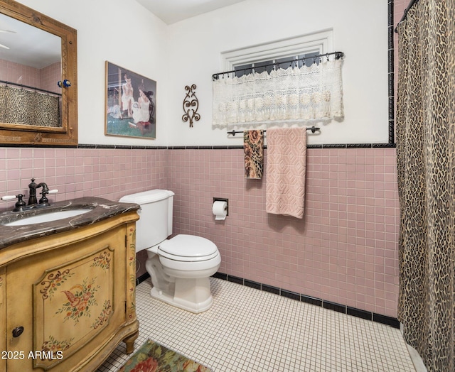 full bath with tile patterned floors, wainscoting, tile walls, toilet, and vanity
