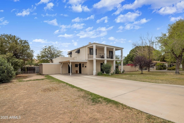 rear view of house featuring stucco siding, fence, a balcony, concrete driveway, and a lawn