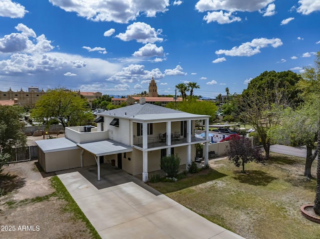 greek revival inspired property with fence, an attached carport, driveway, and a balcony