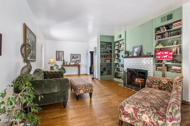 living room featuring wood finished floors, visible vents, and a brick fireplace