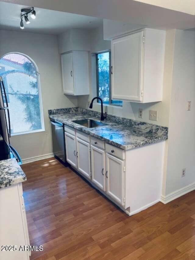 kitchen with a sink, baseboards, stainless steel dishwasher, and dark wood-type flooring