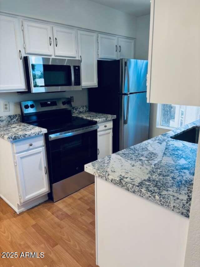 kitchen featuring light wood finished floors, appliances with stainless steel finishes, white cabinets, and light stone countertops