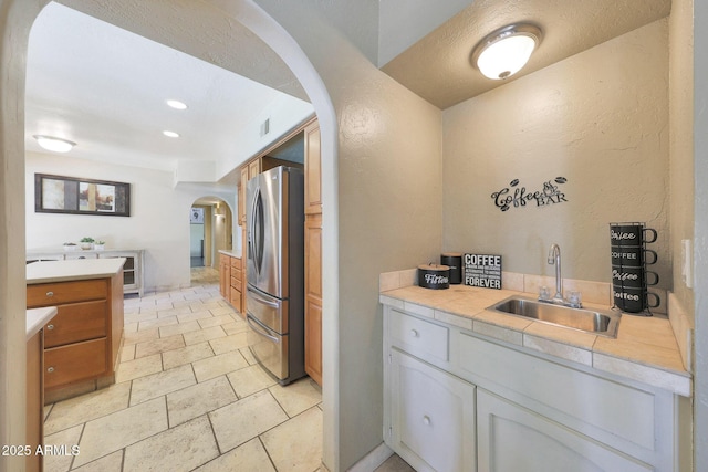 6911 E Thunderbird Rd, Scottsdale, AZ 85254 - kitchen featuring arched walkways, stainless steel refrigerator with ice dispenser, a textured wall, recessed lighting, and light stone finish floors
