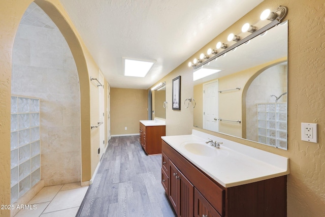 6911 E Thunderbird Rd, Scottsdale, AZ 85254 - bathroom featuring two vanities, a textured wall, wood finished floors, and a tile shower