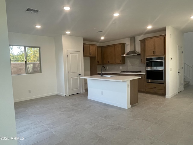 kitchen featuring wall chimney exhaust hood, sink, a center island with sink, stainless steel appliances, and decorative backsplash