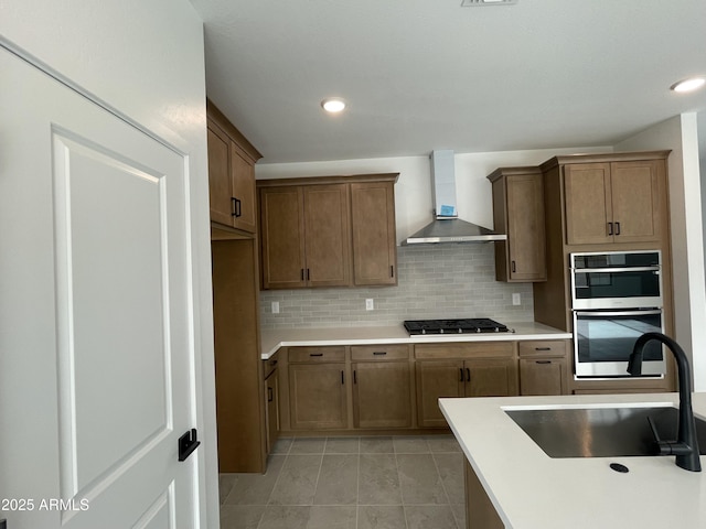 kitchen featuring light tile patterned flooring, sink, backsplash, stainless steel appliances, and wall chimney exhaust hood