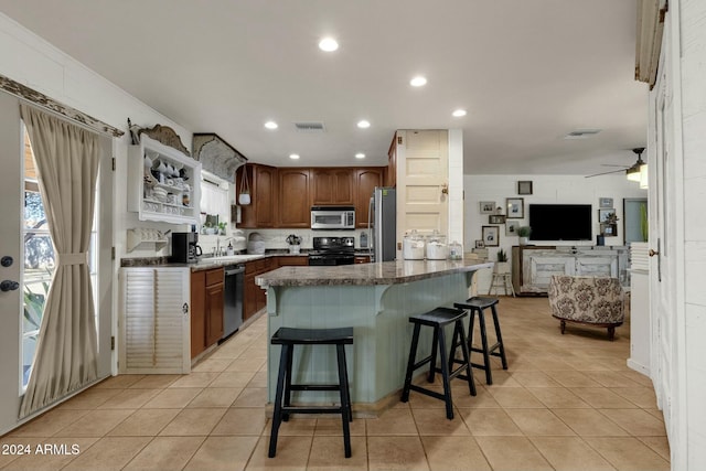 kitchen with a kitchen bar, stainless steel appliances, ceiling fan, light tile patterned floors, and a center island