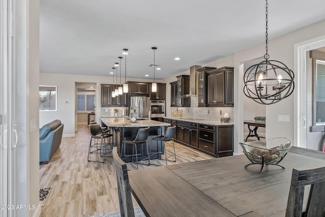 14655 W Pasadena Ave, Litchfield Park, AZ 85340 - kitchen featuring dark brown cabinetry, appliances with stainless steel finishes, a breakfast bar area, backsplash, and a notable chandelier