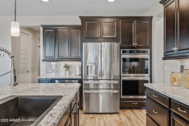 14655 W Pasadena Ave, Litchfield Park, AZ 85340 - kitchen with tasteful backsplash, light wood-type flooring, appliances with stainless steel finishes, dark brown cabinetry, and light stone countertops