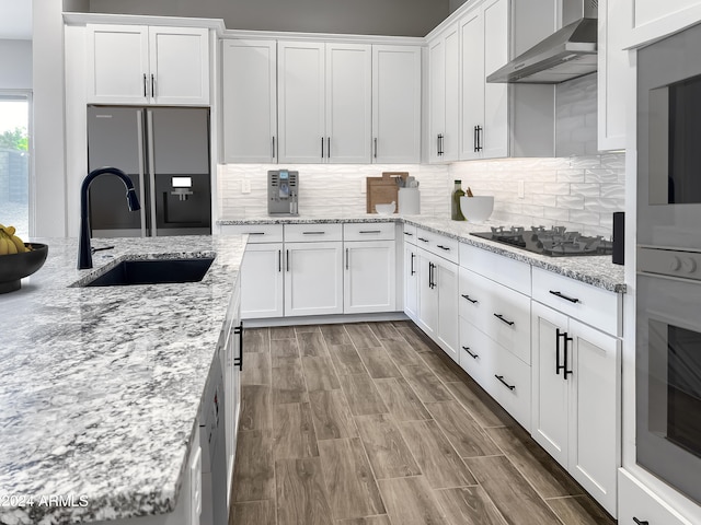 kitchen featuring sink, white cabinetry, wall chimney exhaust hood, stainless steel appliances, and light stone countertops