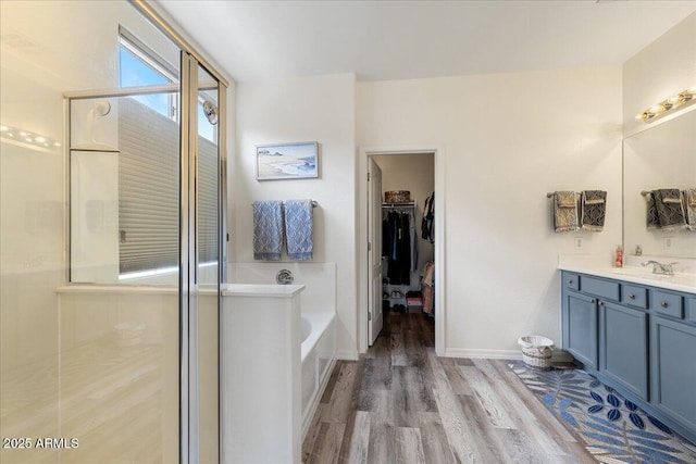 bathroom with a walk in closet, a garden tub, a stall shower, wood finished floors, and vanity