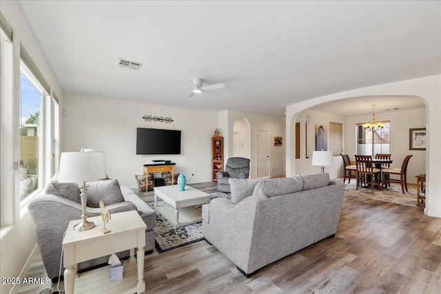 living area with visible vents, arched walkways, wood finished floors, and ceiling fan with notable chandelier