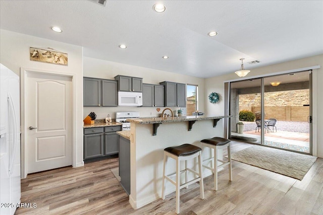 kitchen featuring white appliances, light stone counters, a breakfast bar, light wood-style flooring, and gray cabinetry