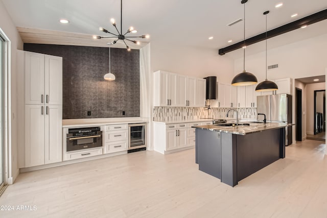 kitchen with beamed ceiling, a center island with sink, pendant lighting, wall oven, and white cabinetry