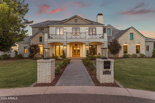 view of front of home with stone siding, french doors, a front lawn, and a balcony