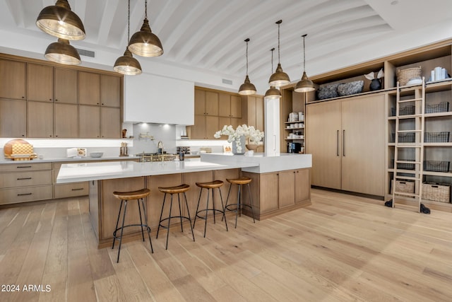 kitchen featuring a kitchen bar, beamed ceiling, decorative light fixtures, light hardwood / wood-style floors, and a large island