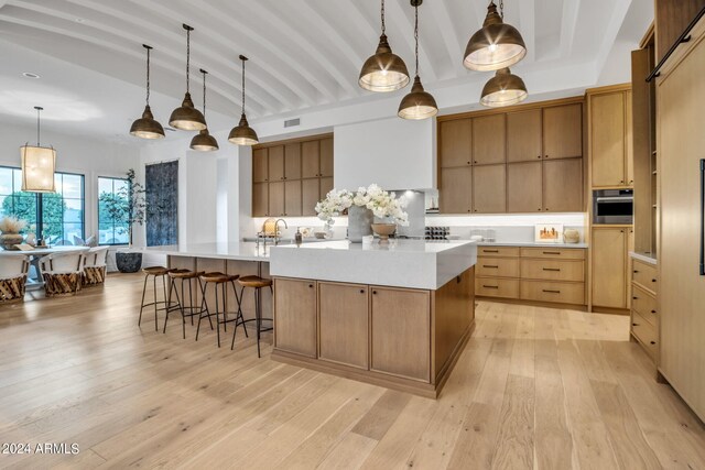 kitchen with stainless steel oven, a spacious island, hanging light fixtures, and light wood-type flooring