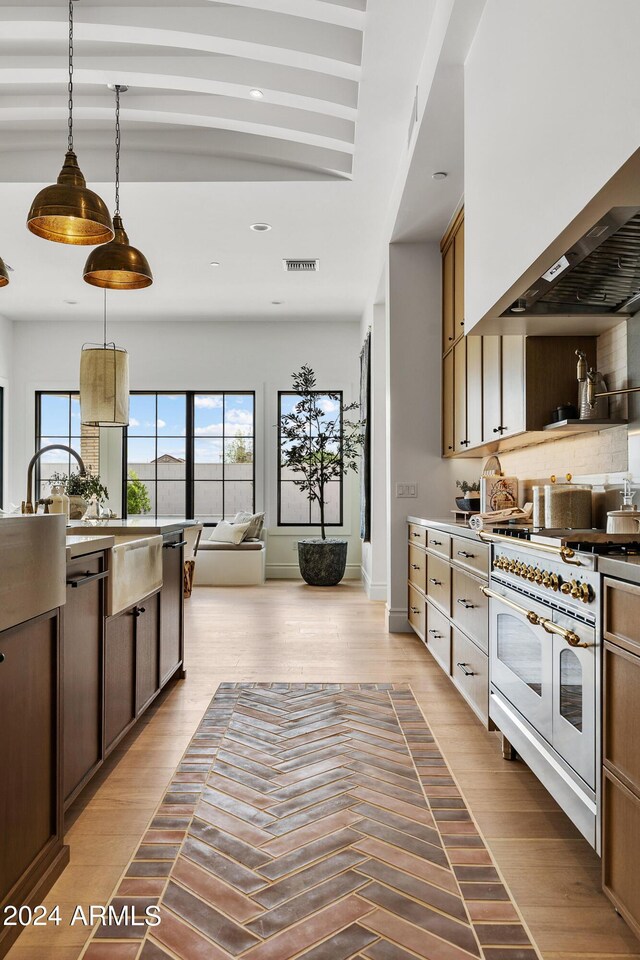 kitchen with wall chimney range hood, double oven range, decorative light fixtures, decorative backsplash, and hardwood / wood-style flooring