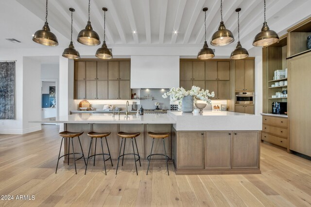 kitchen with beamed ceiling, pendant lighting, a spacious island, and light hardwood / wood-style floors