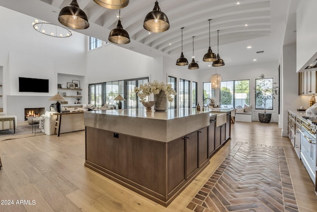 kitchen with light hardwood / wood-style flooring, a high ceiling, a kitchen island with sink, hanging light fixtures, and dark brown cabinetry