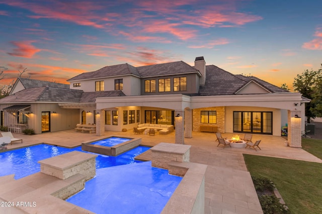 back of house at dusk featuring an outdoor living space with a fire pit, a patio, a chimney, an in ground hot tub, and an outdoor pool