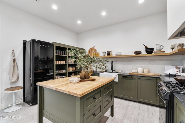 kitchen with green cabinets, gas stove, butcher block counters, decorative backsplash, and sink