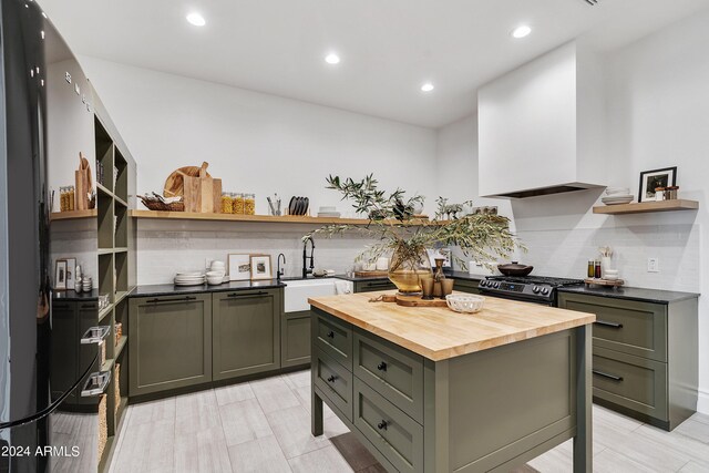 kitchen with butcher block countertops, sink, backsplash, custom exhaust hood, and black gas stove