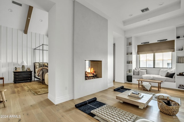 living room featuring beam ceiling, light hardwood / wood-style floors, and built in features